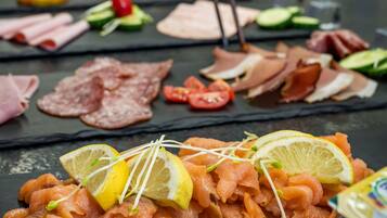 Diversos alimentos como salmón ahumado, verduras y carnes dispuestos sobre una superficie de pizarra negra.