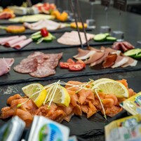 Diversos alimentos como salmón ahumado, verduras y carnes dispuestos sobre una superficie de pizarra negra.