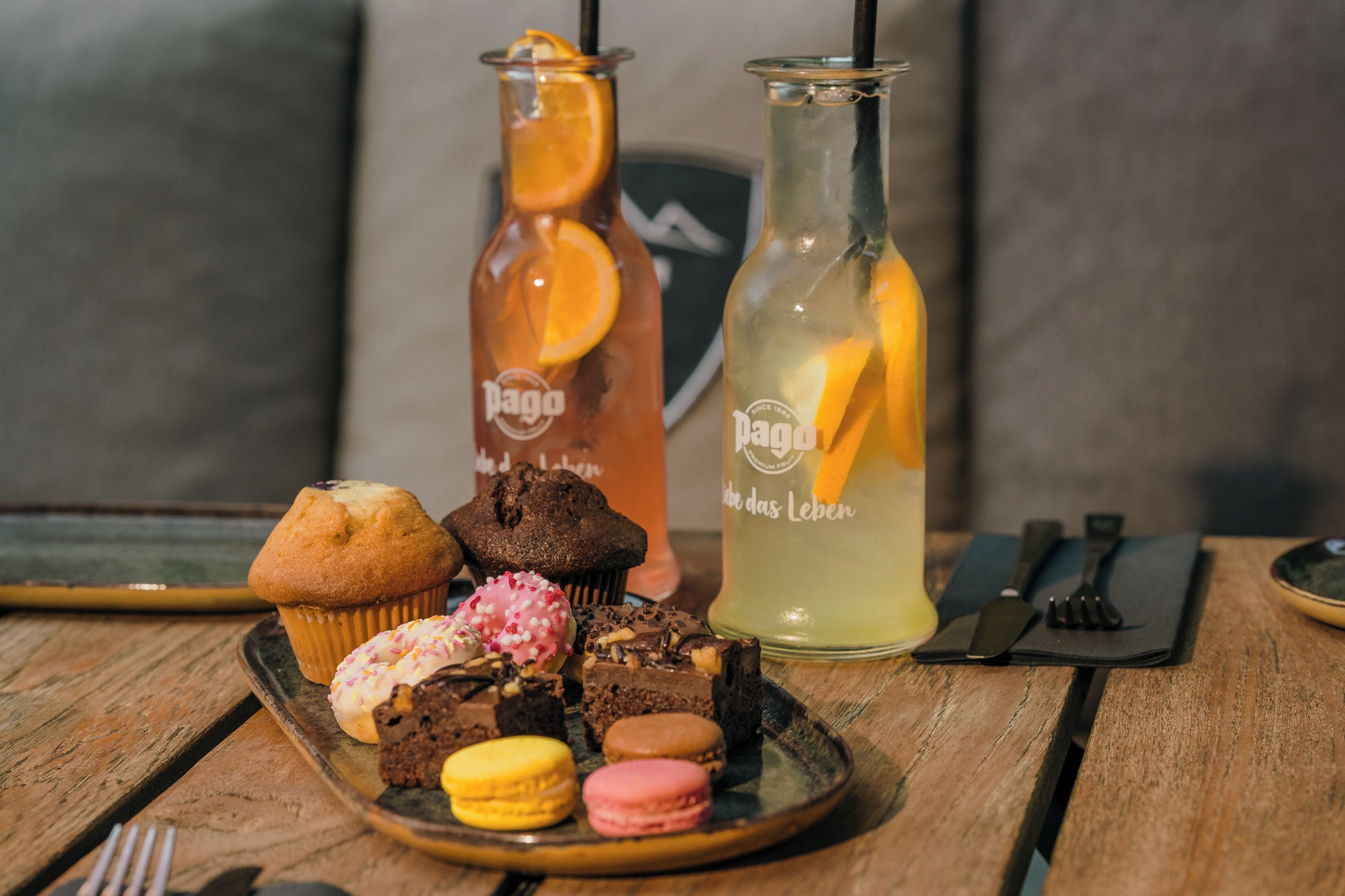 Een houten tafel met een bord gebak, twee flessen drank en een set servetten.