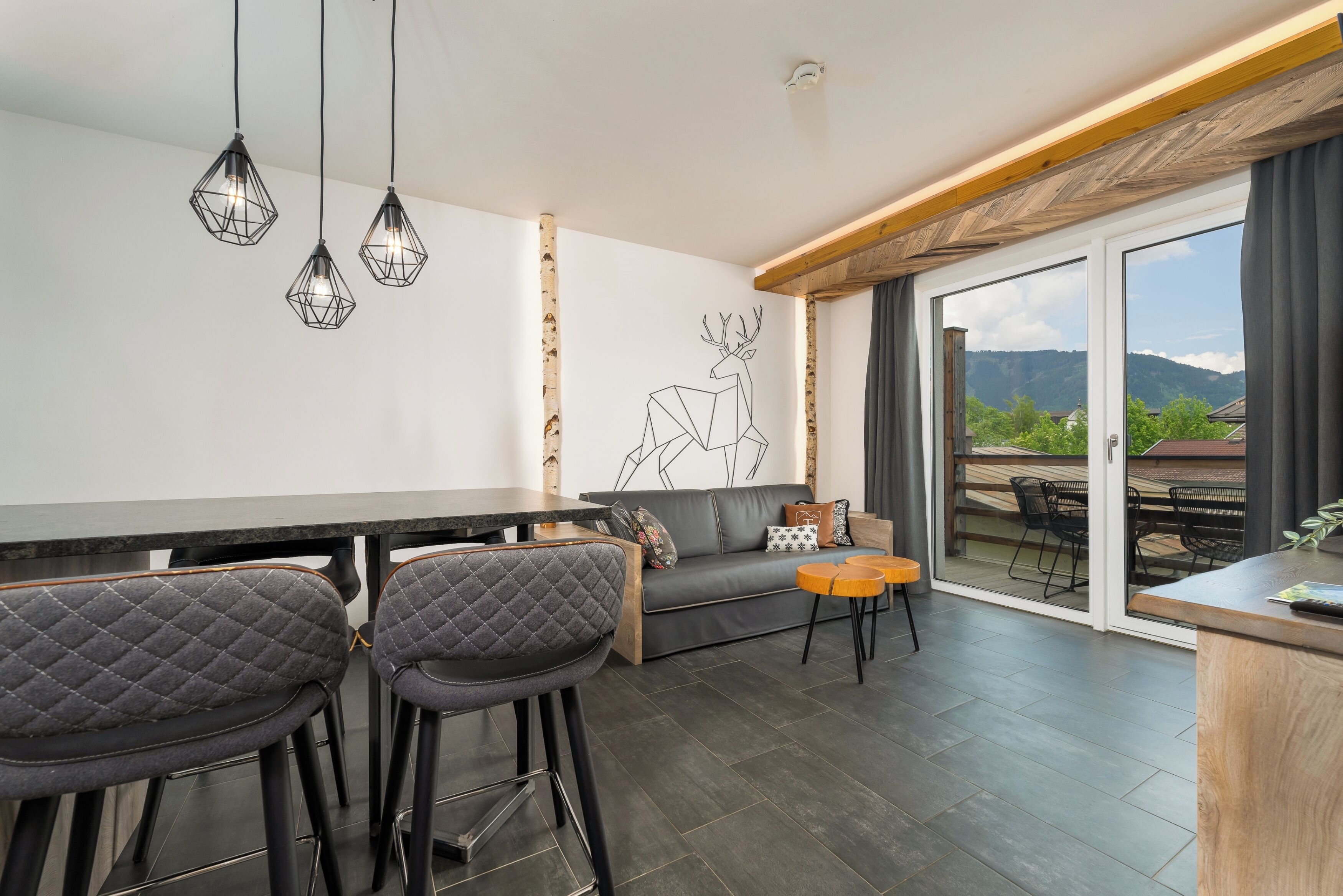A modern kitchen with a bar area, a dining space with a sofa and chairs, and a large sliding glass door leading to an outdoor patio.