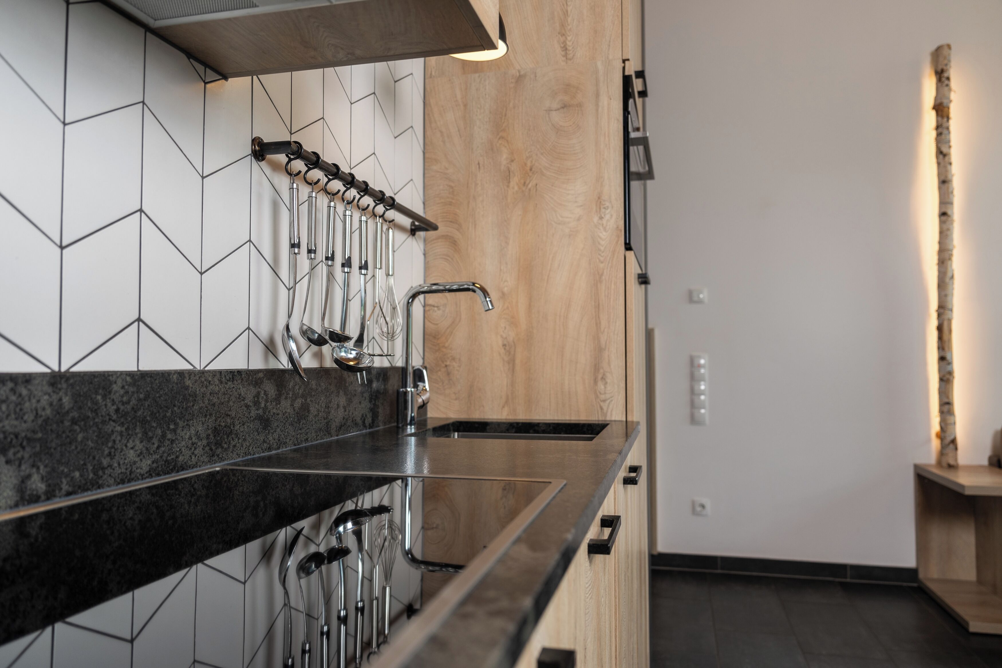 A modern kitchen with a black granite countertop, a wooden backsplash, and a hanging faucet.