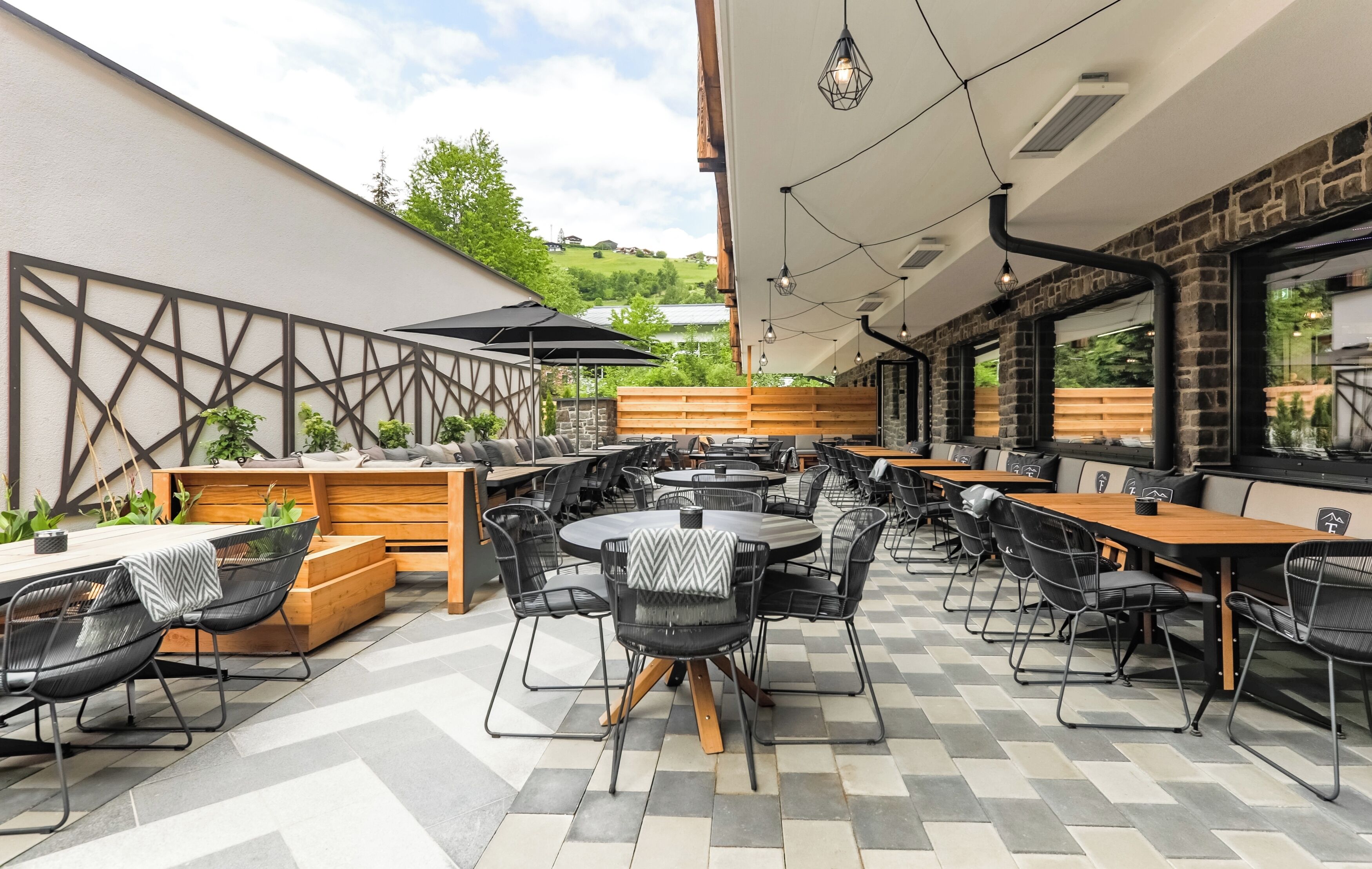An outdoor dining area with multiple tables and chairs, wooden benches, and a checkered floor.