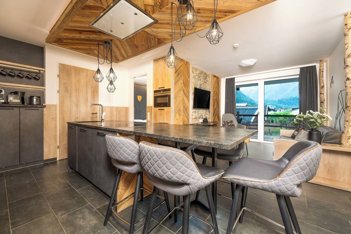 A modern kitchen with a central island, bar stools, and a large window offering a mountain view.