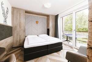 A modern bedroom with a large bed, a wooden headboard, and a view of the outdoors through a sliding glass door.