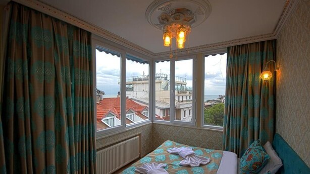 A hotel room with a bed, curtains, a chandelier, and a view of buildings through large windows. - Paris Garden Hotel Istanbul (Istanbul)