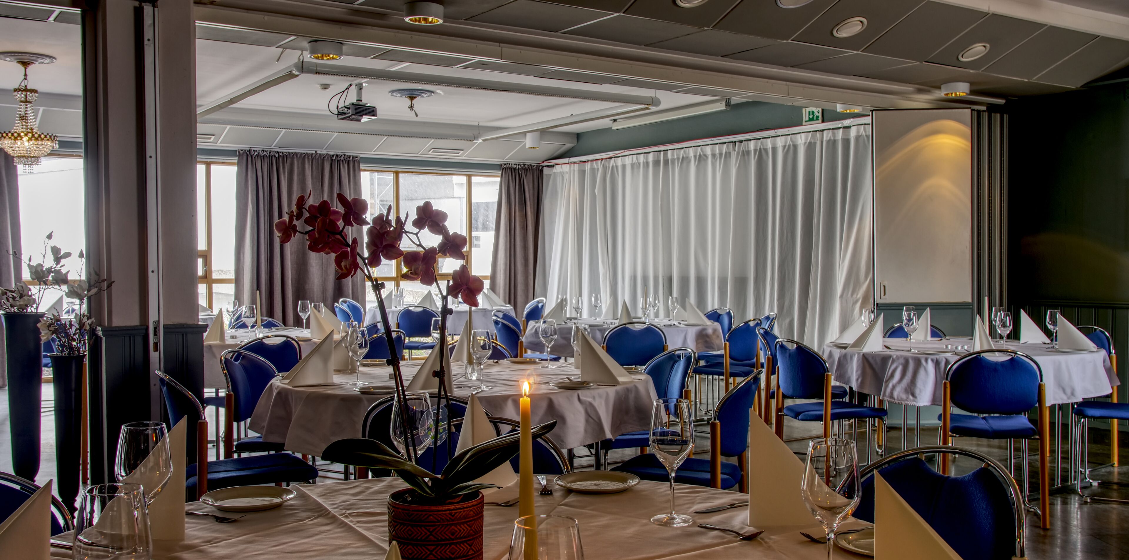 Ein Restaurant mit blauen Stühlen, weißen Tischdecken und Kerzen auf den Tischen.