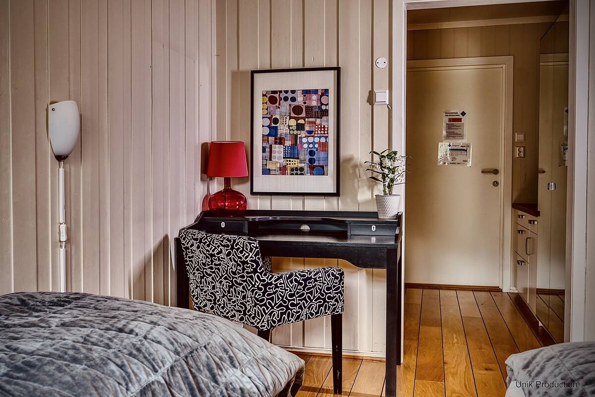 Hotelkamer met een bed, een bureau met rode lamp, een gestreept stoel en een kunstwerk in een lijst aan de muur.
