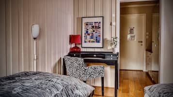 Una habitación de hotel con una cama, un escritorio con una lámpara roja, una silla estampada y una obra de arte enmarcada en la pared.