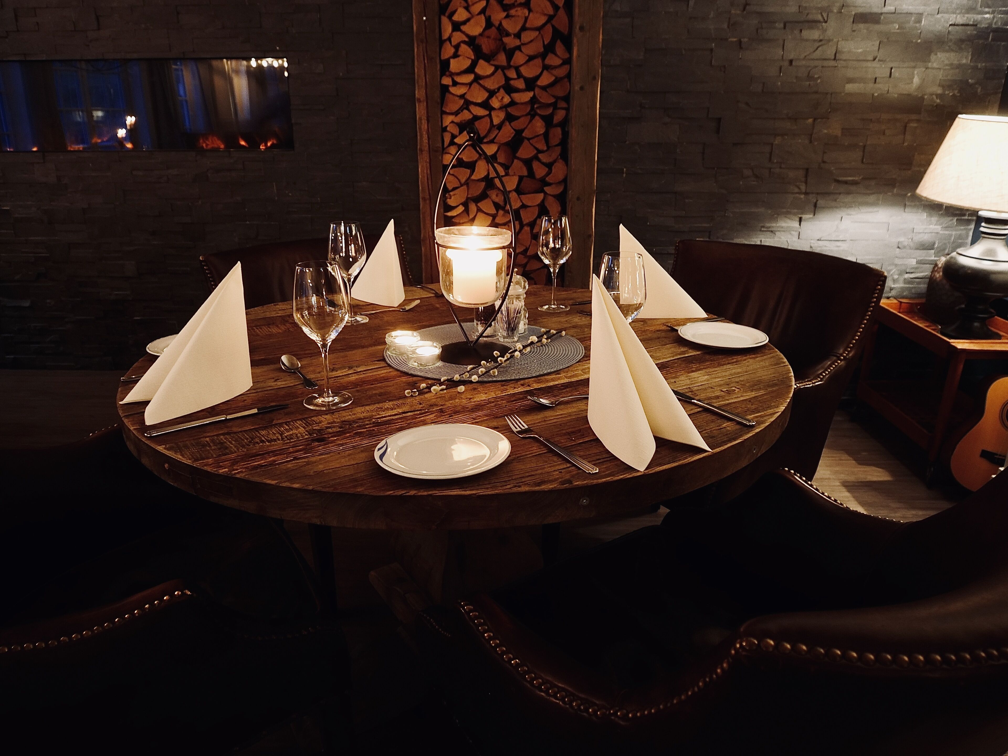 A round dining table set for four with white napkins, wine glasses, and a candle centerpiece.