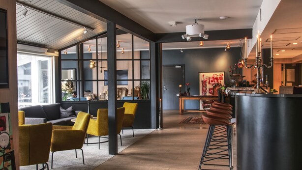 Een modern interieur met een bank, gele stoelen, een groot raam en een keuken met een fornuis.