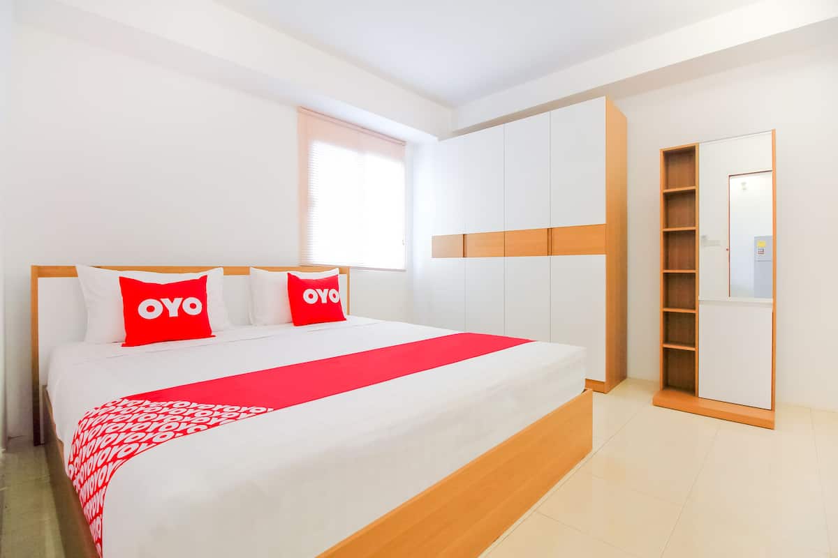 Ein Hotelzimmer mit einem großen Bett, weißen Wänden, einem Holzkopfstück und einem Schrank mit Spiegel.