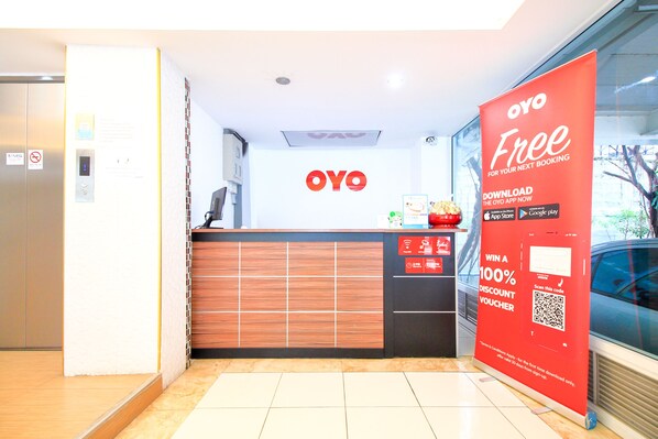 Zona de recepción de hotel con un mostrador de madera, una pantalla digital y un banner promocional rojo.