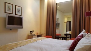 A hotel room with a bed, a TV mounted on the wall, a desk with a chair, and a mirror.