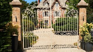 A gated entrance with wrought iron gates and stone pillars, leading to a brick building with a pitched roof. - Manoir des Lions de Tourgéville (Tourgeville)