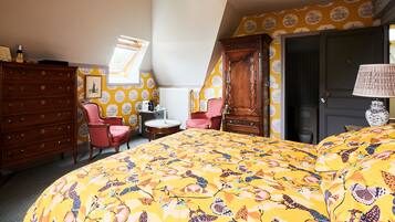 A bedroom with a bed, two chairs, a dresser, a lamp, and a window with a view.