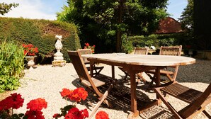 A wooden outdoor dining table with chairs, surrounded by gravel, with red flowers in the foreground. - Manoir des Lions de Tourgéville (Tourgeville)