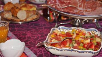 A table with a variety of food items including a fruit salad, bread, and a dish with sliced meat.