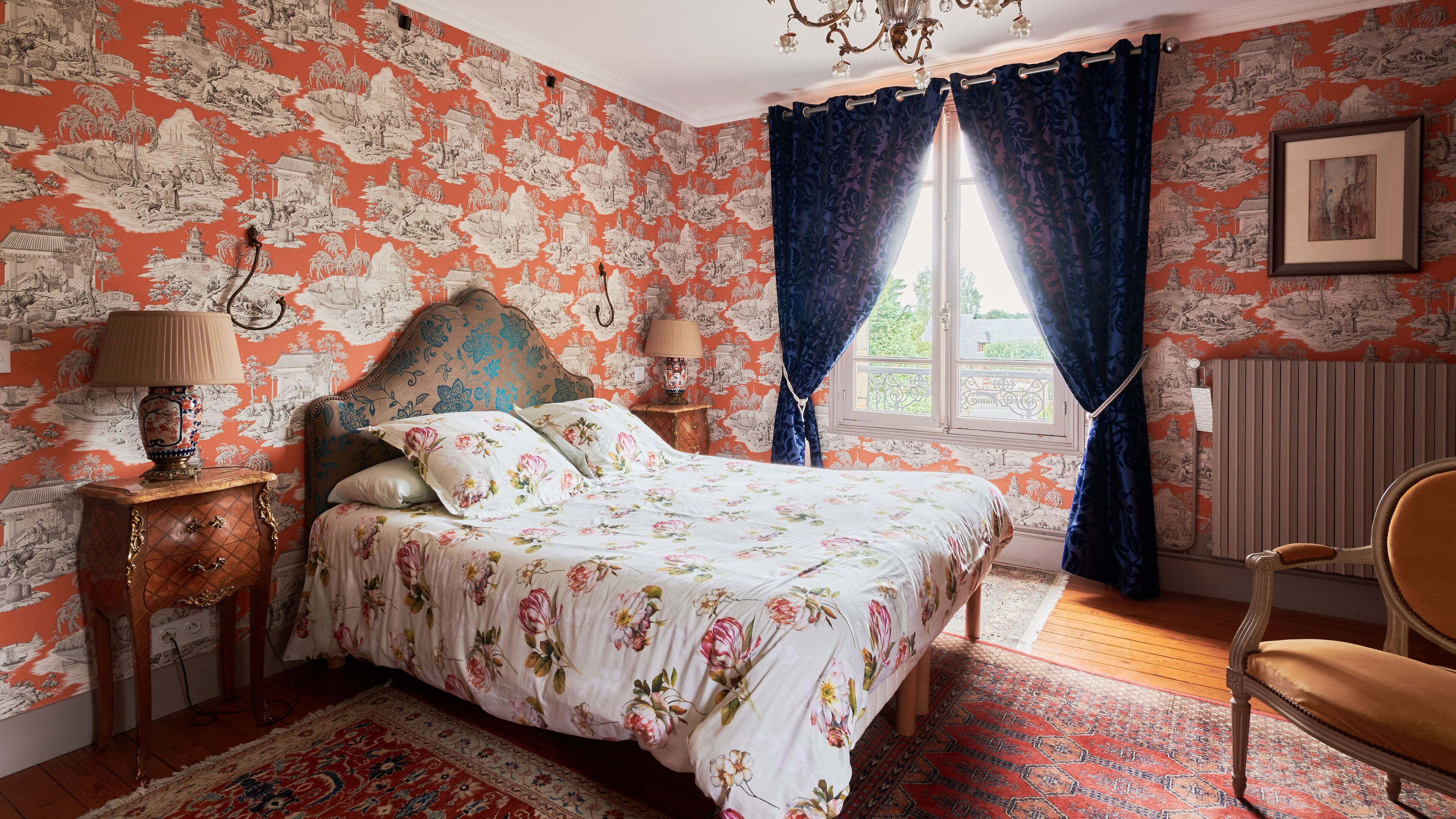 A bedroom with a bed, a nightstand, a chair, and a window with curtains.