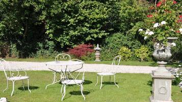 A garden with a white metal table and chairs, surrounded by lush greenery and a decorative urn.