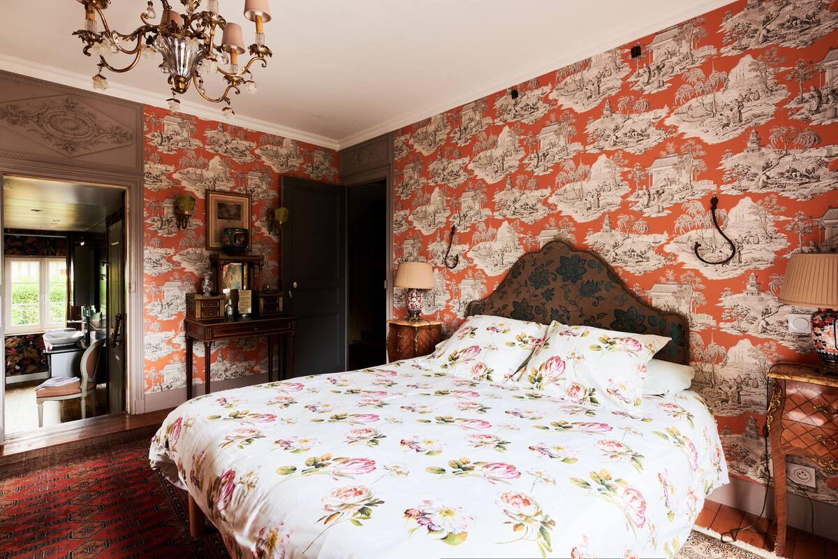 Ein Schlafzimmer mit floraler Bettdecke, einem Chandelier und einer Wand mit rotem und weißem Muster.