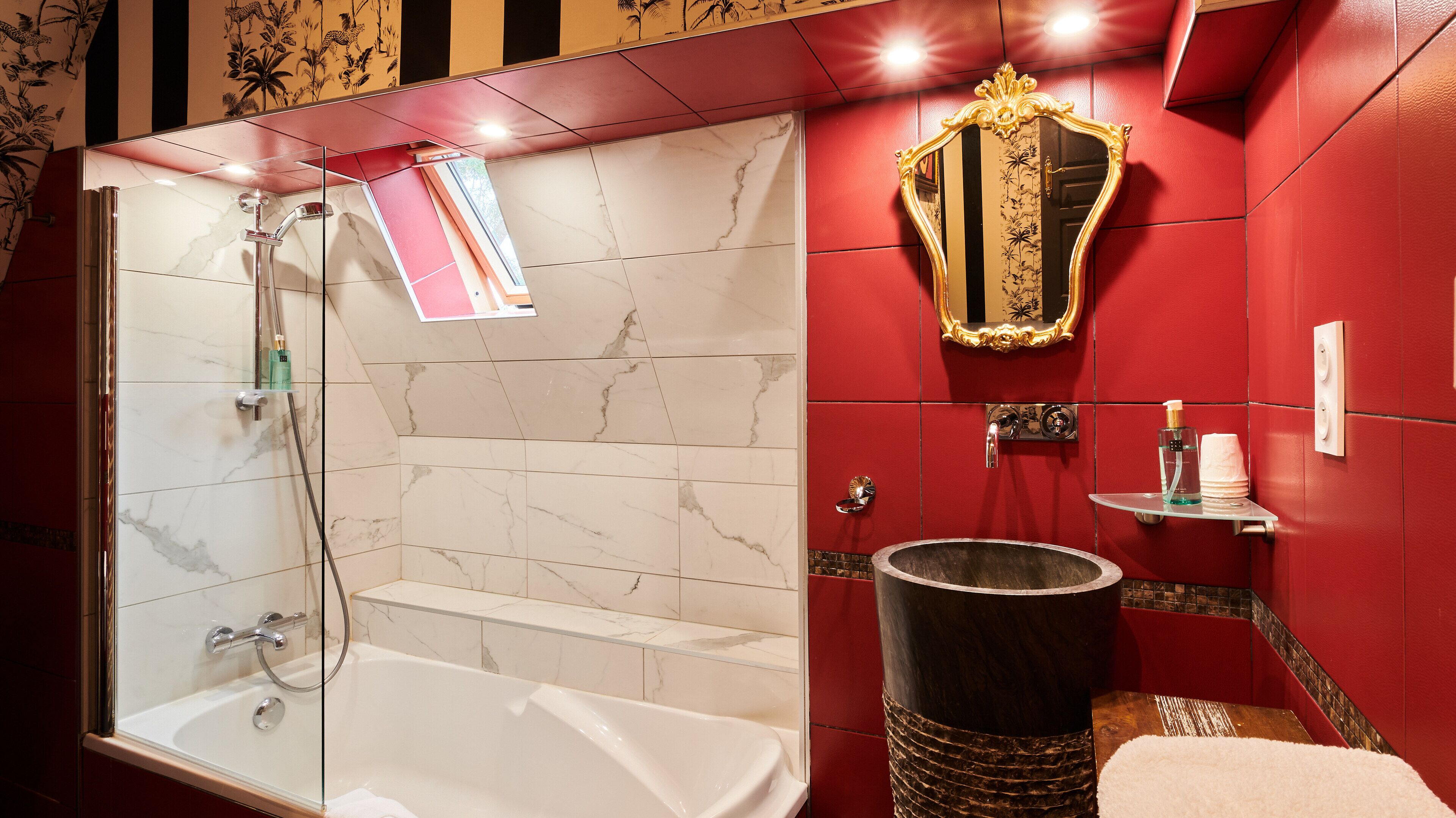 A bathroom with a glass-enclosed shower, a marble-tiled wall, a vanity with a mirror, and a sink.