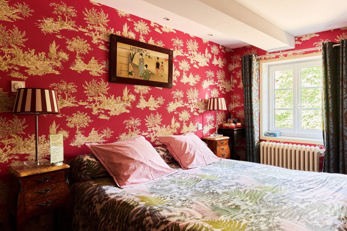 Ein Schlafzimmer mit einem Bett, zwei Nachttischlampen, einer Kommode, einem Fenster mit Vorhängen und einem Heizkörper.