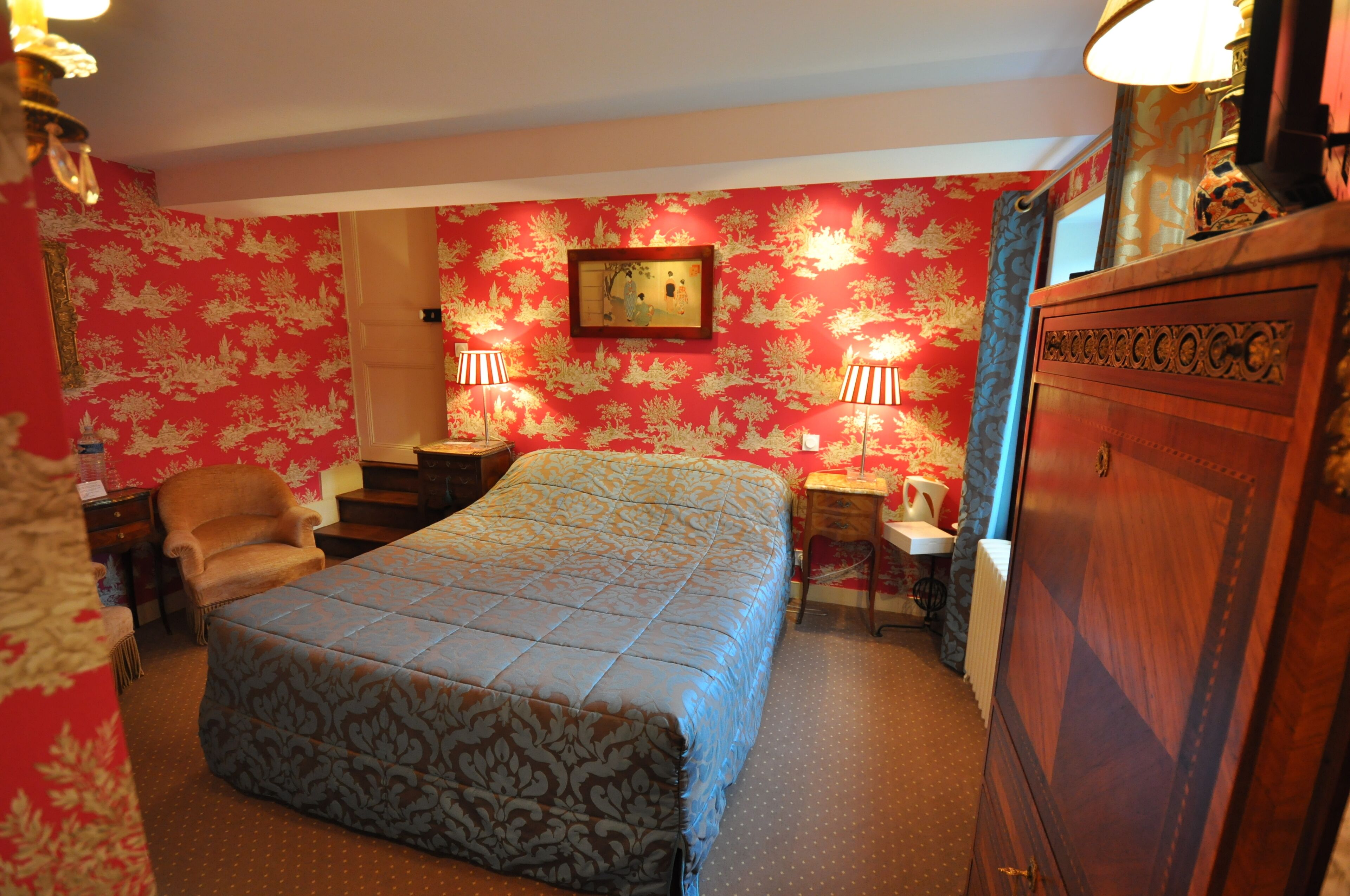 A hotel room with a large bed, two bedside tables with lamps, a chair, a dresser, and a framed picture on the wall.