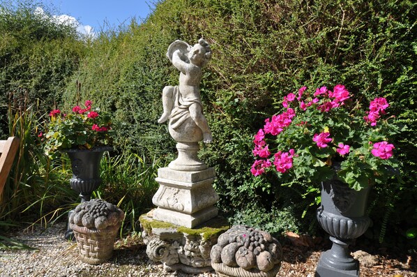 Un jardín con una estatua de piedra, plantas en macetas y abundante vegetación.