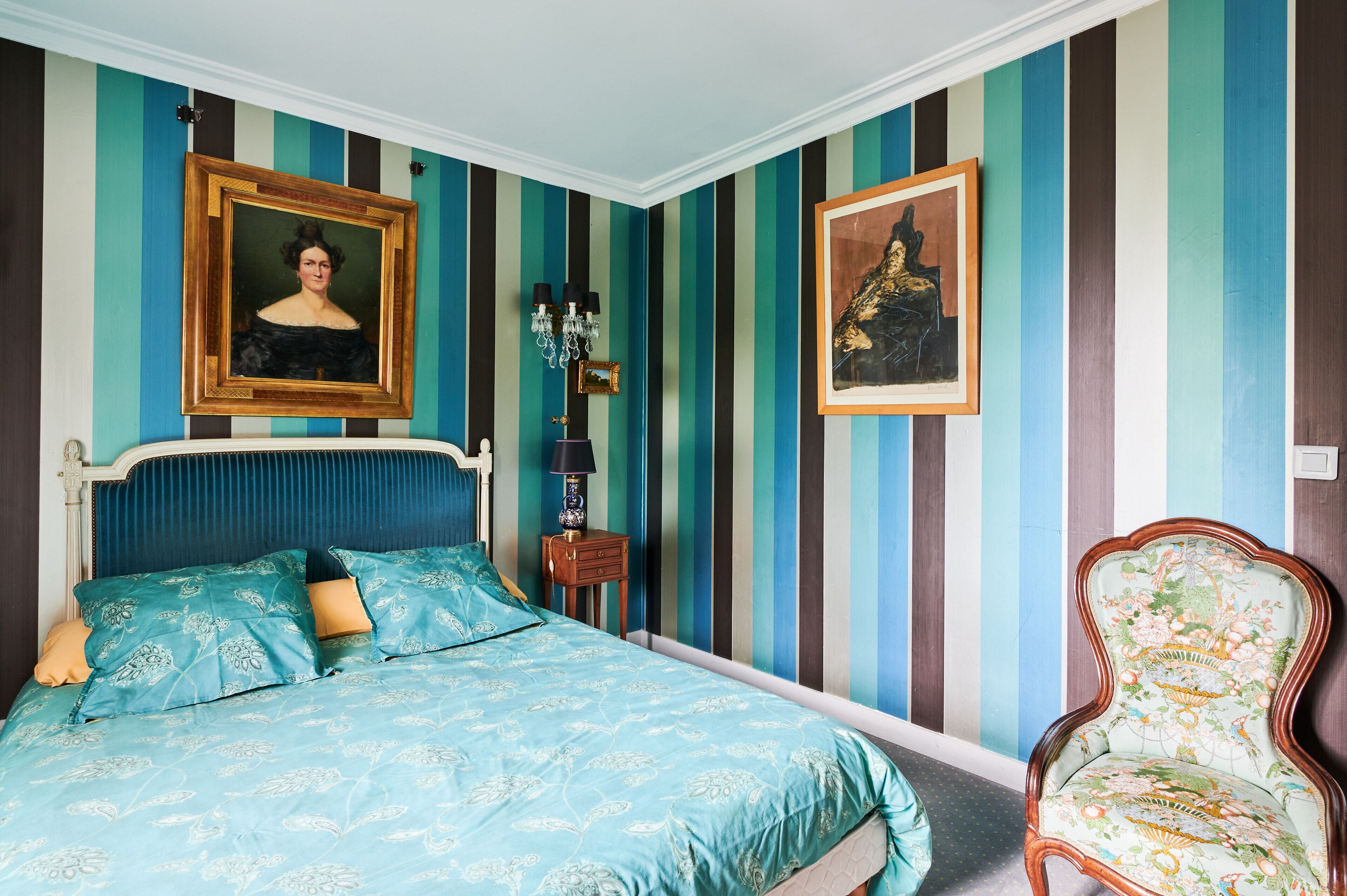 A bedroom with a bed, a nightstand, a chair, and two framed pictures on the wall.