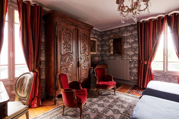 Ein Zimmer mit einem großen Holzschrank, zwei roten Polsterstühlen, einem Bett mit weißer Bettwäsche und einem gemusterten Teppich.