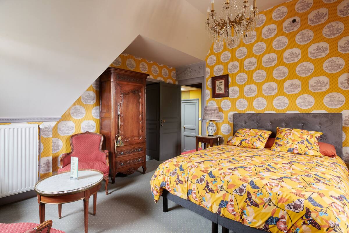 Ein Schlafzimmer mit einem großen Bett, einer Holzkommode, einem roten Sessel und einem Kronleuchter.