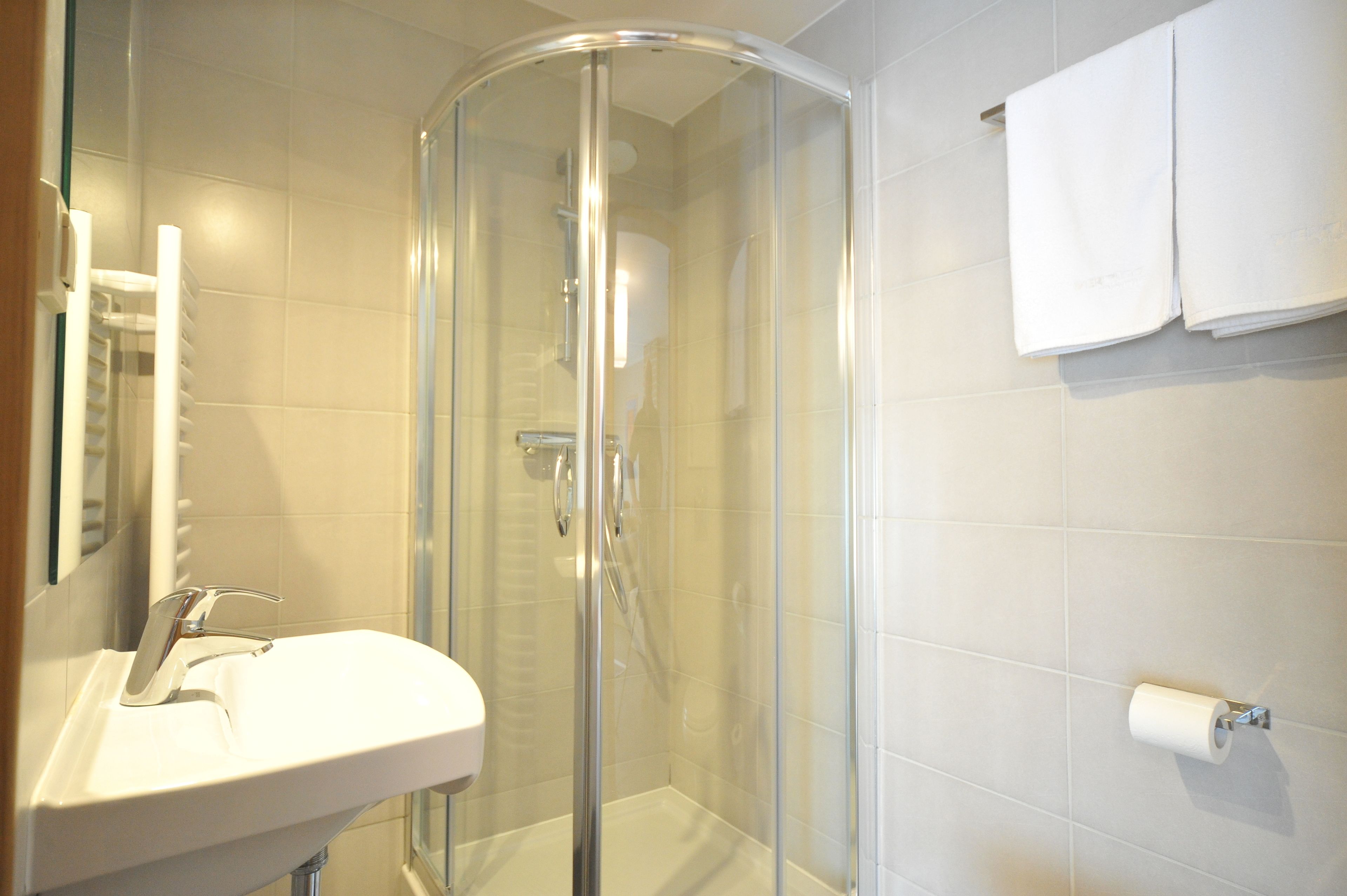 Een badkamer met een douchecabine van glas, een wastafel en een toiletrolhouder.