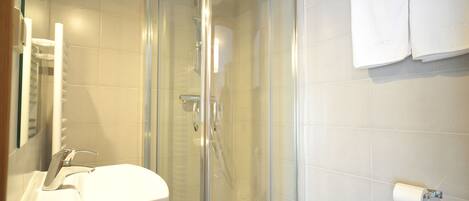 Een badkamer met een douchecabine van glas, een wastafel en een toiletrolhouder.
