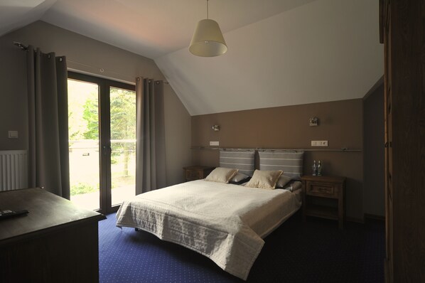 A bedroom with a large bed, a desk, a hanging light fixture, and a view of the outdoors. - Vertigo Narie (Morag)