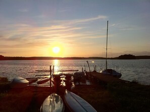 A sunset over a calm lake with boats docked at a wooden pier. - Vertigo Narie (Morag)