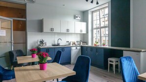 Una cocina moderna con armarios blancos, un lavamanos y un ventanal. Hay dos sillas azules y una mesa con una maceta de flores rosadas.