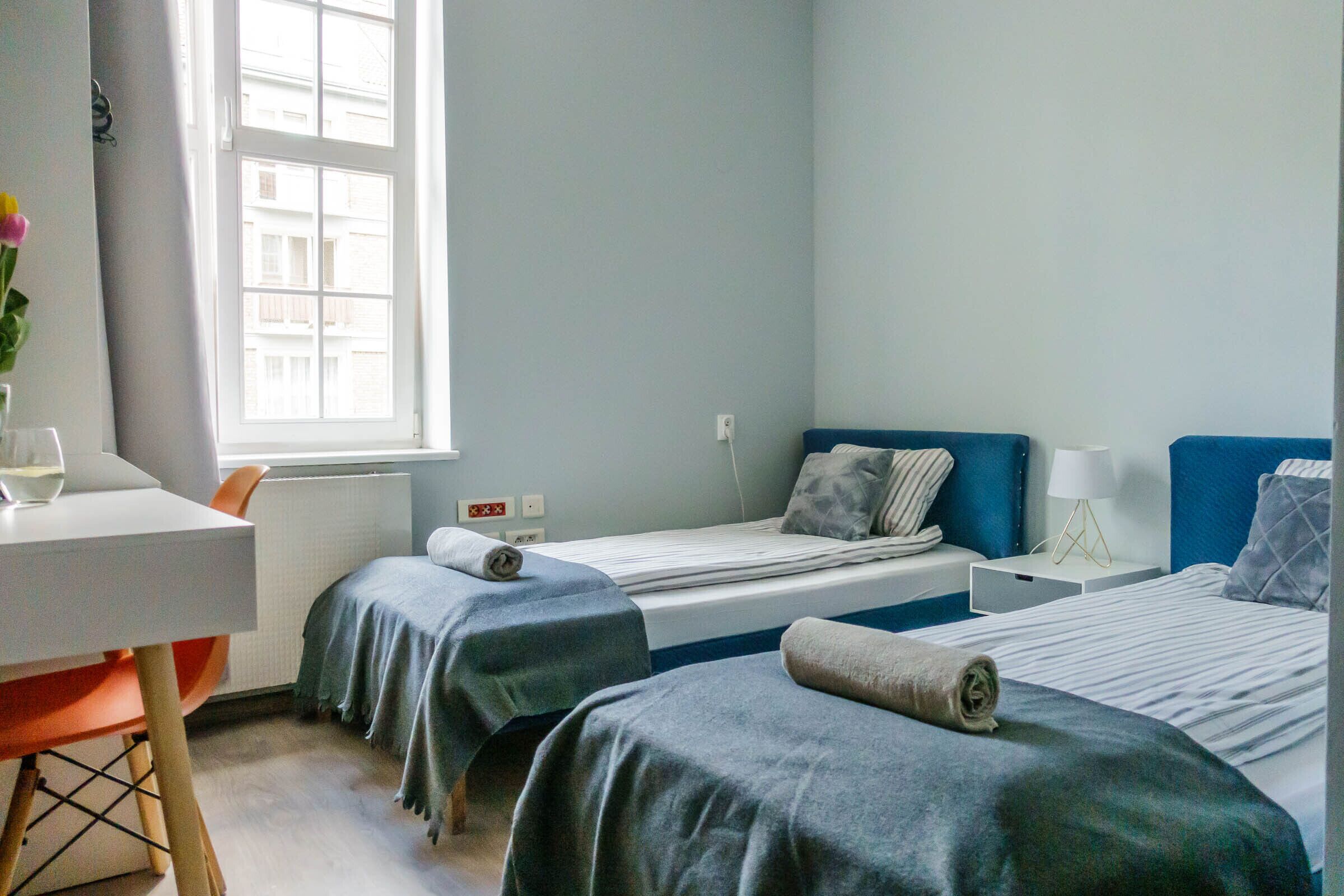 Habitación de hotel con dos camas individuales, un escritorio con silla, una ventana y un radiador.