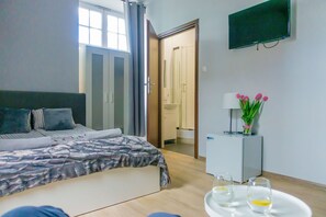 A modern hotel room with a bed, a TV, a small table with glasses, and a door leading to a bathroom. - Trip & Hostel (Gdansk)