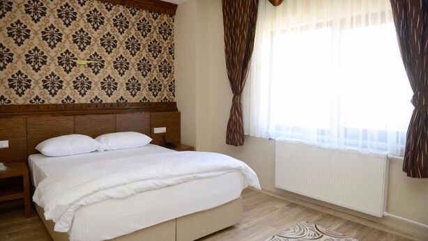 Una cama bien hecha con cabecera, mesita de noche y ventana con cortinas.