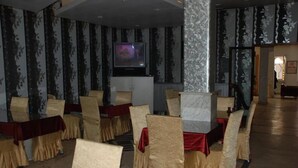 Un salón de conferencias con filas de sillas y mesas, una pantalla de televisión y papel tapiz estampado.