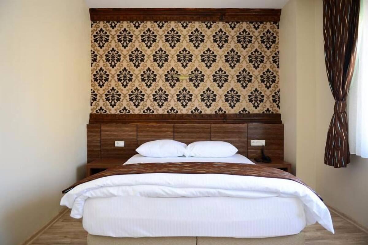 A hotel room with a bed, wooden headboard, and patterned wallpaper.