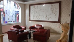 Una habitación con un ventanal grande, sillones de cuero rojo, una mesita y una escultura.