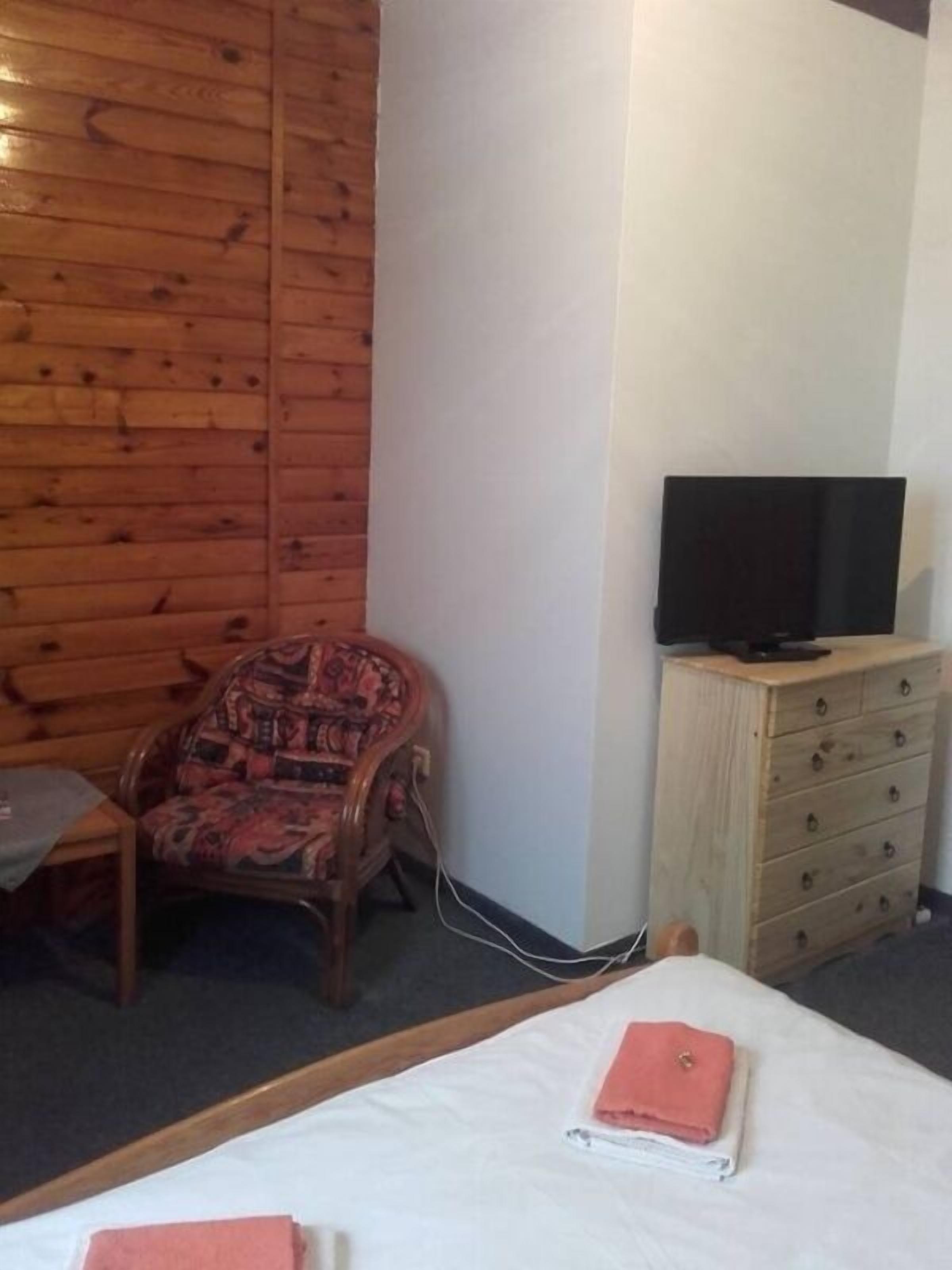 Una habitación con una cama, una silla de madera, un televisor sobre un aparador de madera y un panel de madera en la pared.