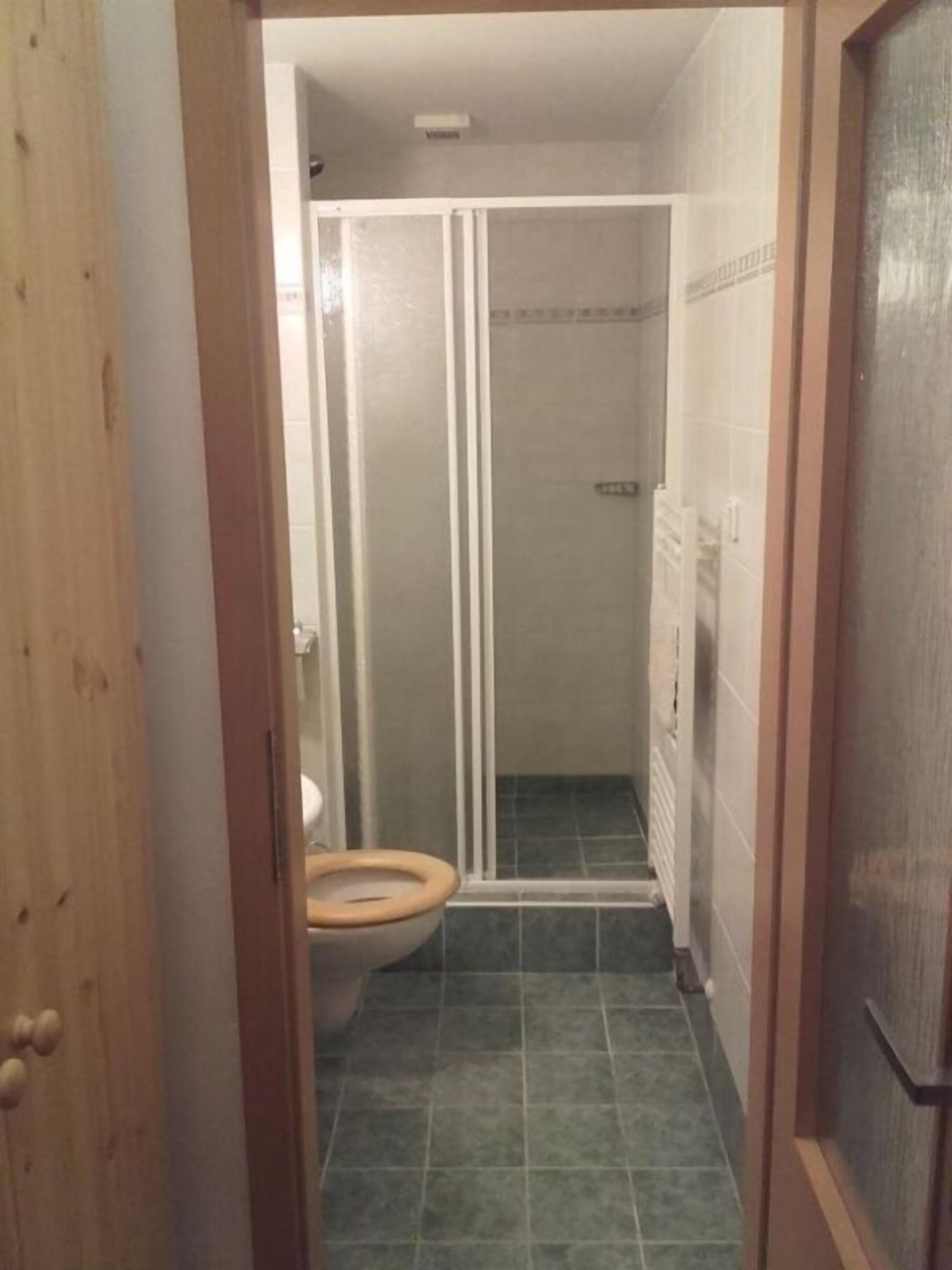 A bathroom with a toilet, a shower enclosure, and a tiled floor.