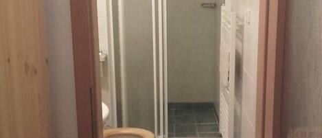 A bathroom with a toilet, a shower enclosure, and a tiled floor.