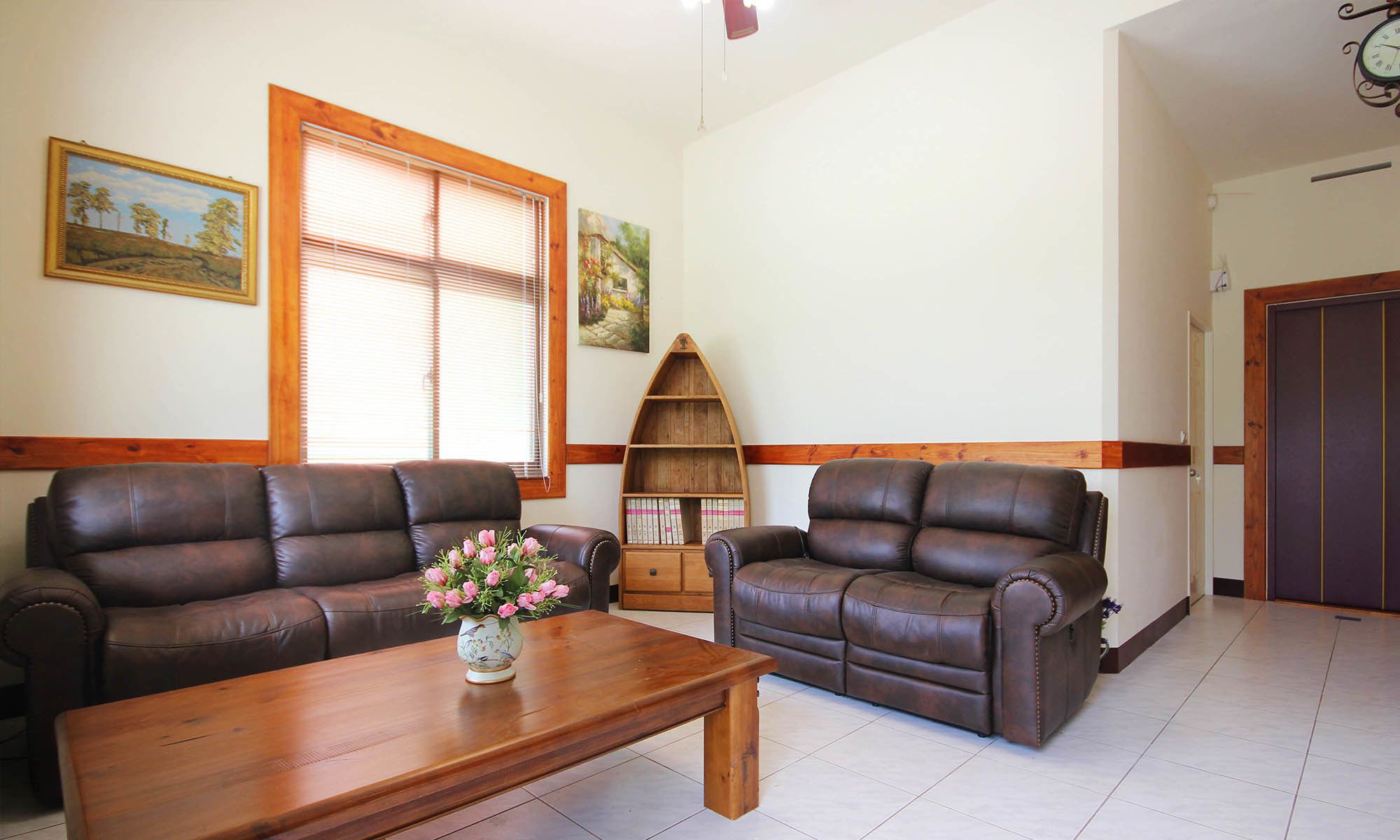A living room with two brown leather sofas, a wooden coffee table, and a bookshelf.