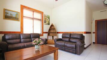 A living room with two brown leather sofas, a wooden coffee table, and a bookshelf.