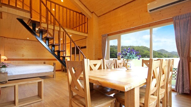 A wooden cabin with a staircase, a dining area with chairs, a table, and a bed. - Taomilou (Puli)