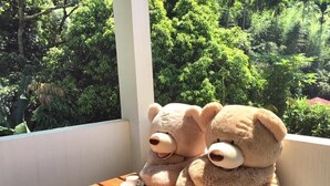 Two teddy bears sitting on a wooden table with cups, overlooking a lush green garden. - Taomilou (Puli)