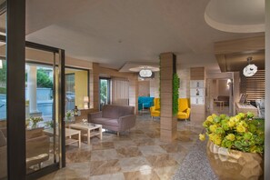 A modern lobby with a checkered floor, a sofa, two armchairs, a coffee table, and a large planter with flowers. - Marina Sands Bijou Boutique Hotel - All Inclusive (Obzor)